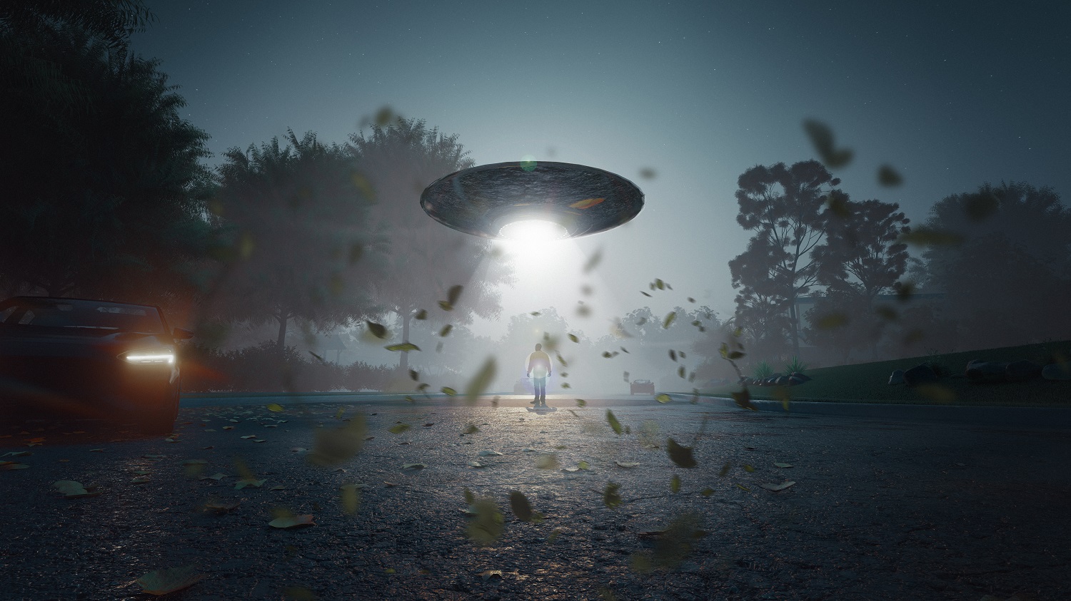 Mężczyzna stoi na środku jezdni, w nocy, w snopie jasnego światła rzucanego przez unoszące się tuż nad nim UFO